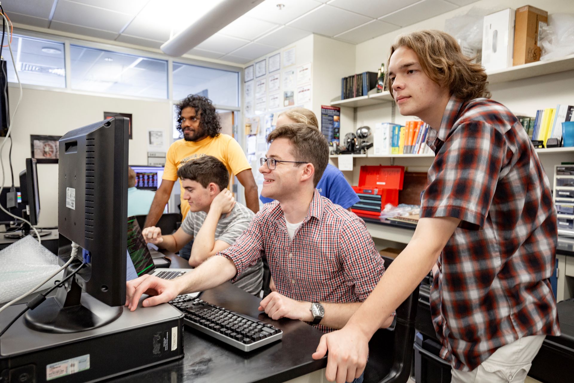 Two students collaborating on a project, one holding a hard drive and the other sitting at a computer